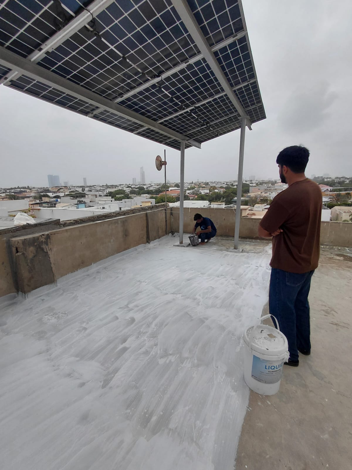 Technician applying liquid PU membrane around solar-panel roof supports